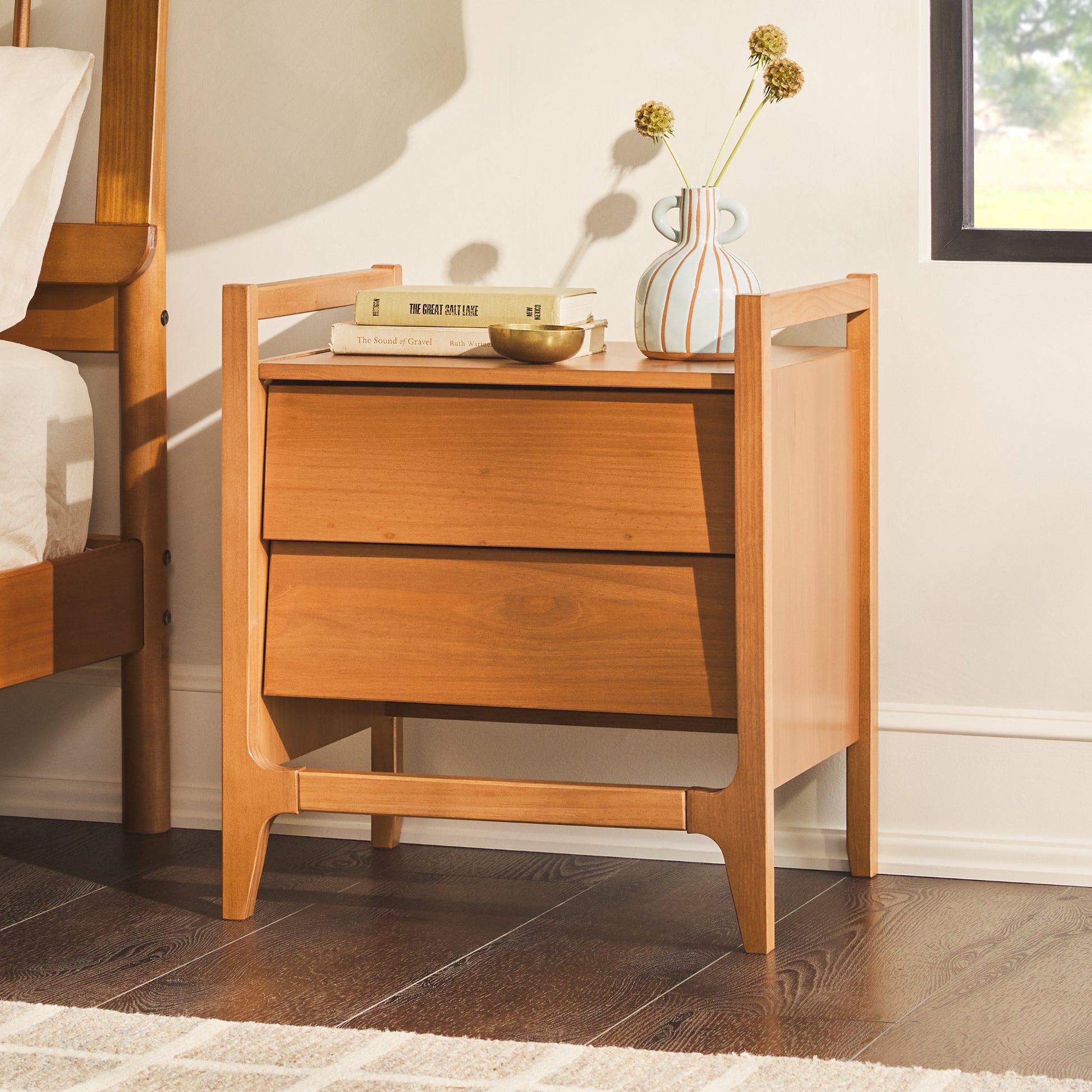 Scandi Angle Face Solid Wood Nightstand in a room, featuring a vase with flowers, a book, and a single drawer with angled fronts.