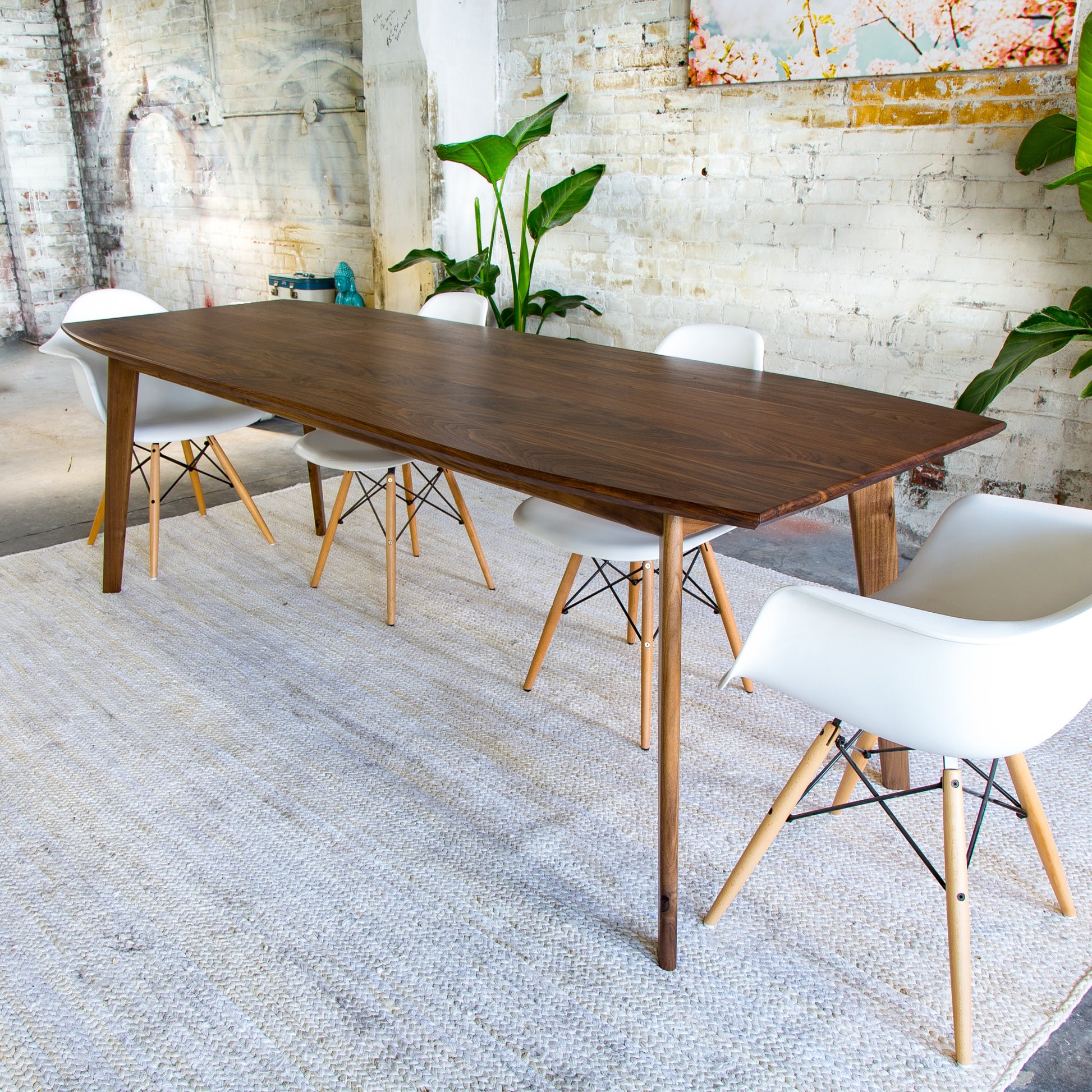 This walnut dining table features a sleek, mid-century design with a contemporary twist, ideal for stylish interiors.
