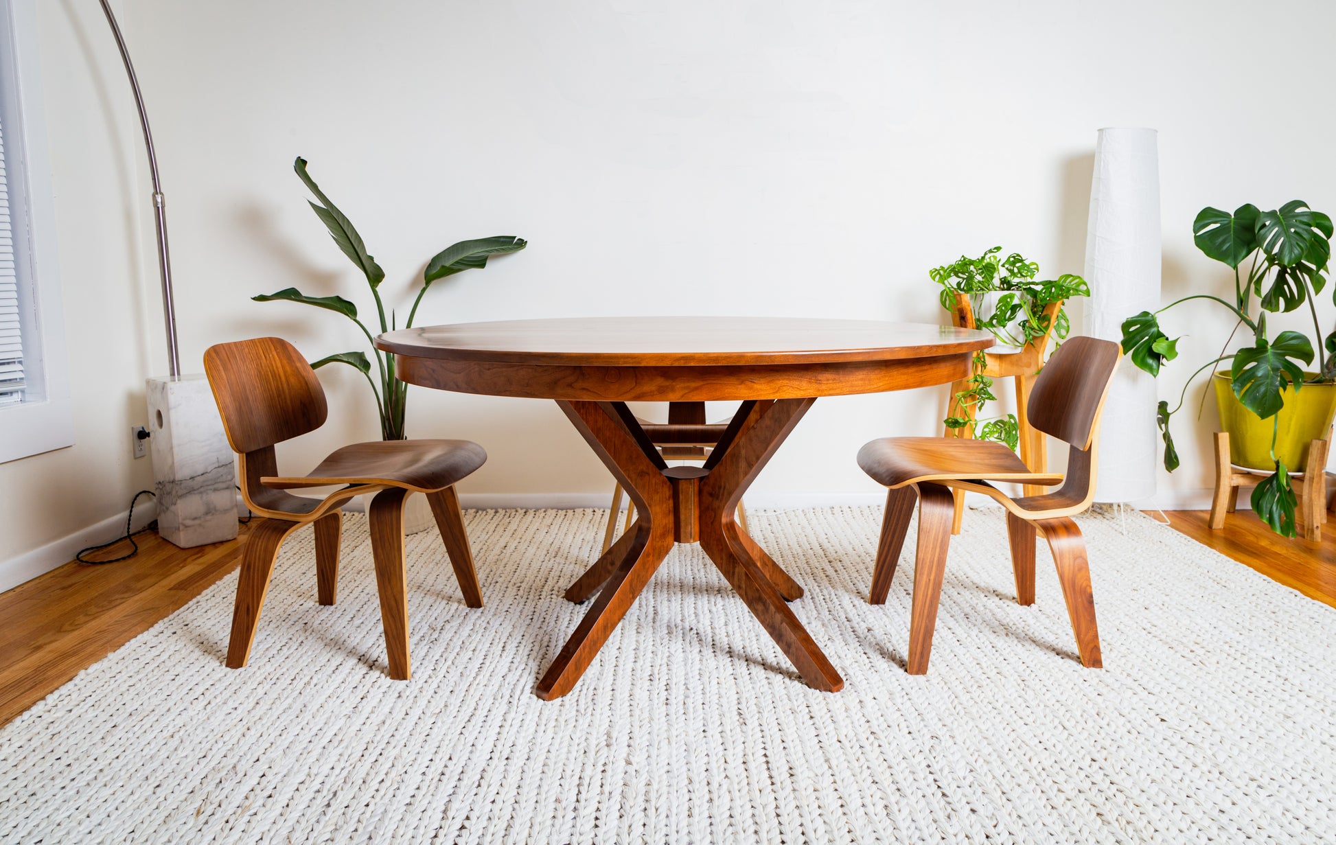 The Corcovado: Modern Small Dining Table for 4 to 8, Extendable, shown in a stylish room with chairs and a potted plant.