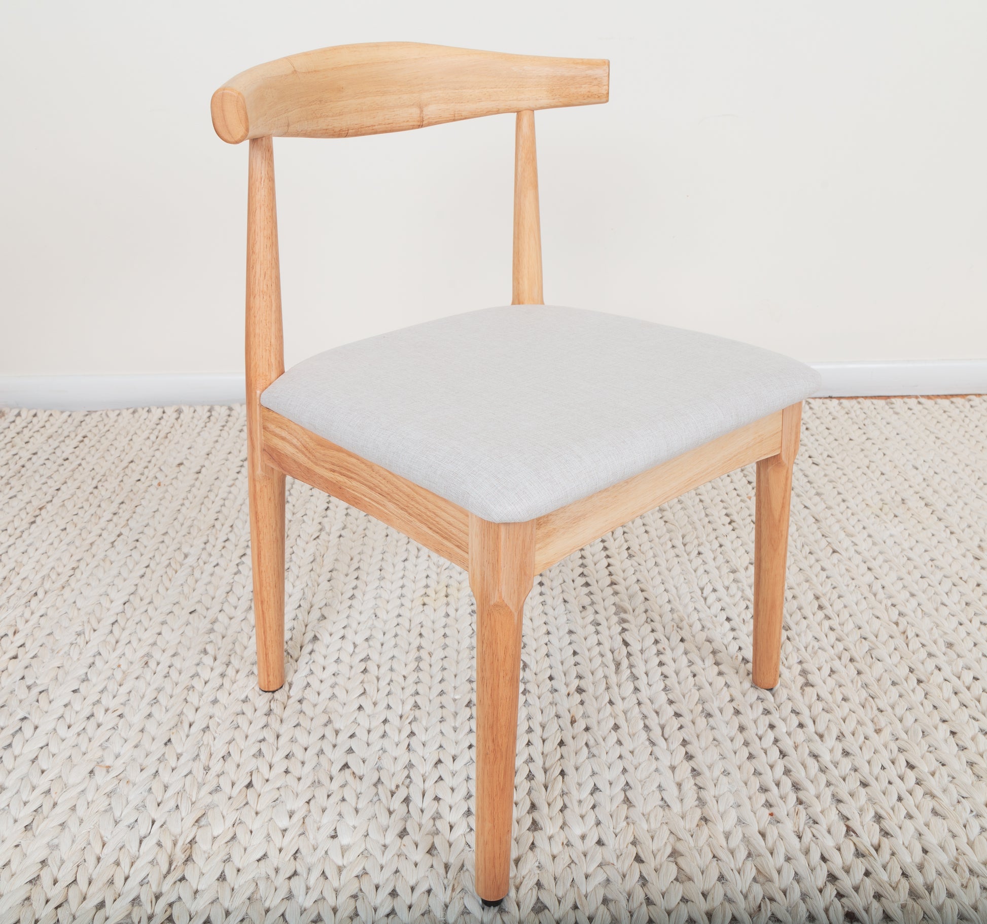 Mid-Century Modern Dining Chair on a rug, showcasing its Ox Chair-inspired curved backrest and parawood construction, perfect for contemporary dining spaces.