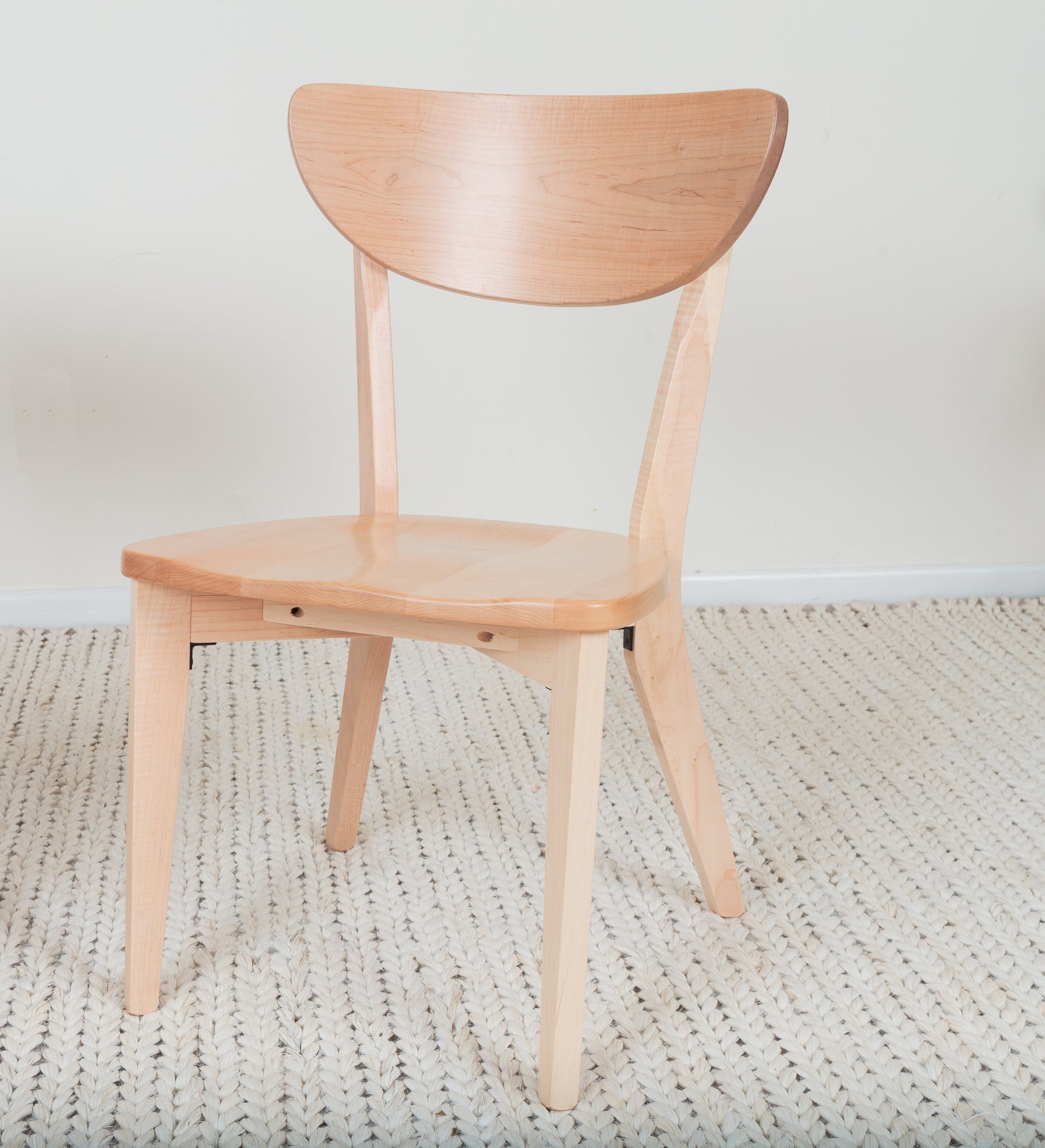 The Seymour - Modern Dining Chair, a handcrafted wooden chair with a curved back, shown on a rug, exemplifying elegant design and solid hardwood construction.