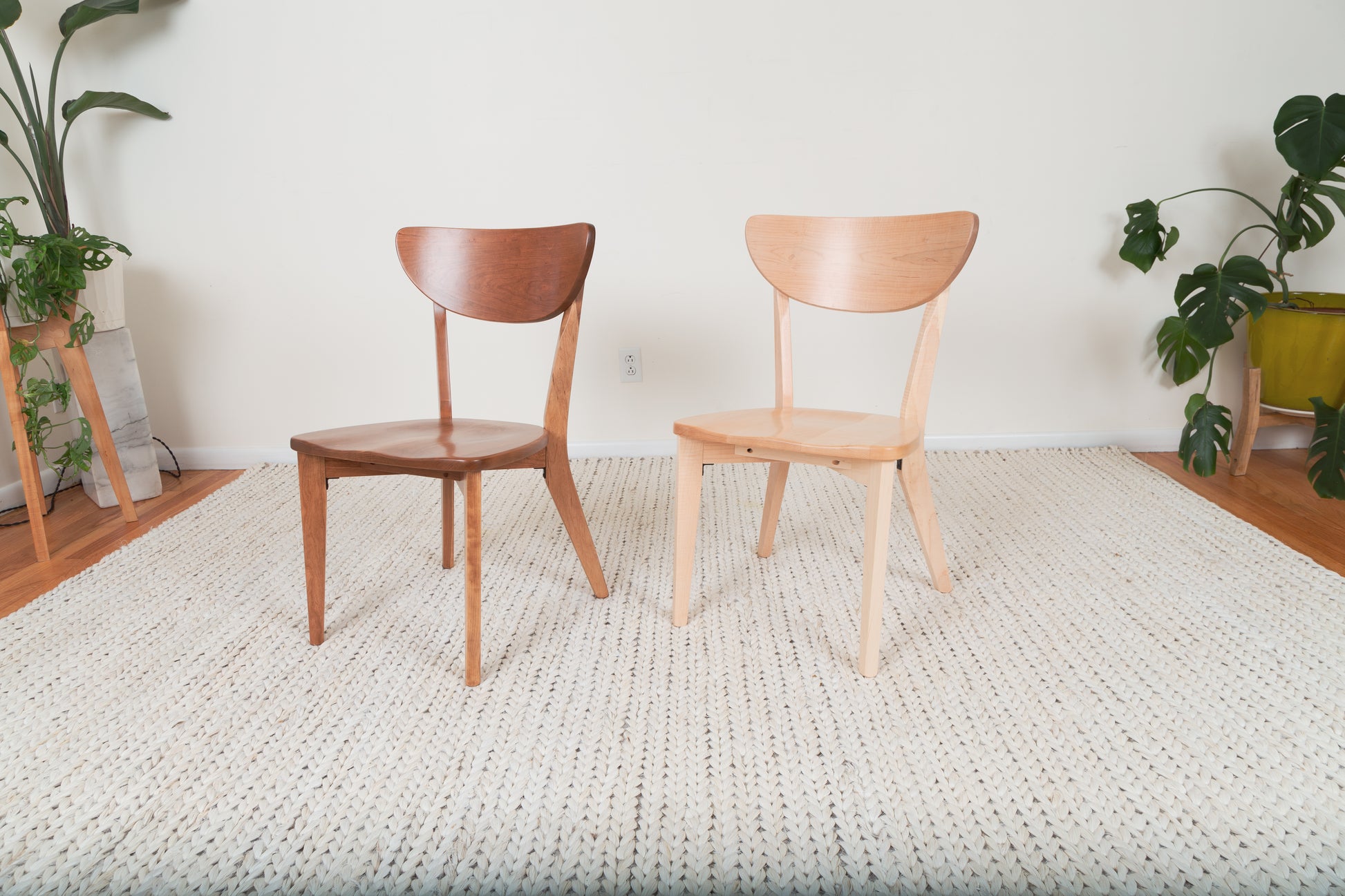 The Seymour - Modern Dining Chair on a woven rug, next to a potted plant, showcasing its sleek, solid wood craftsmanship and modern design.